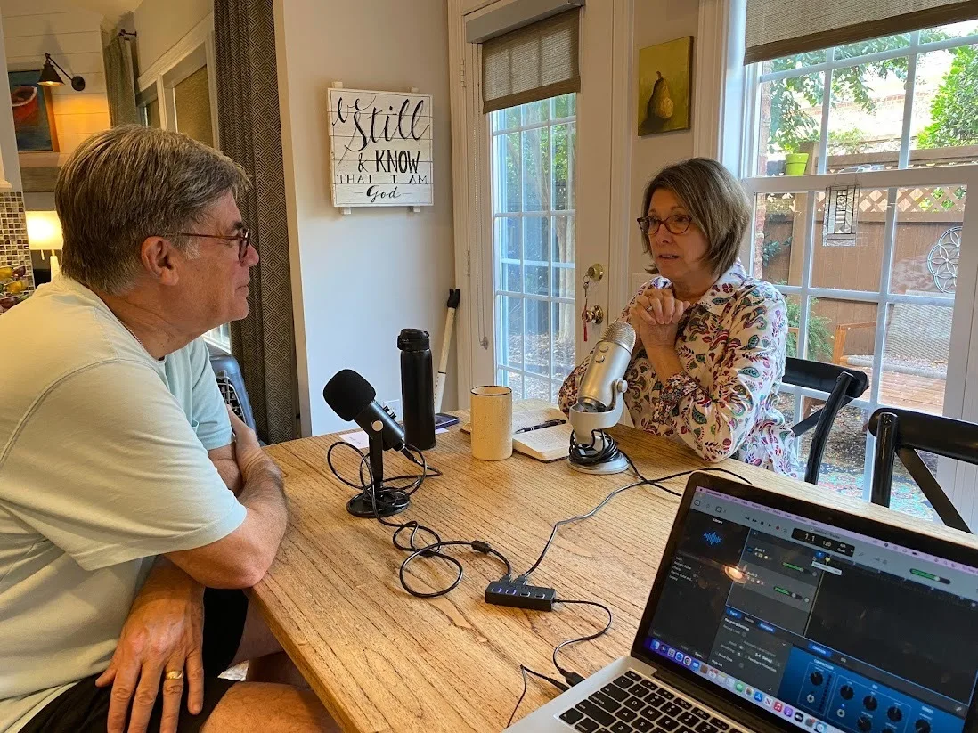 Two podcast hosts in conversation at a table with microphones.